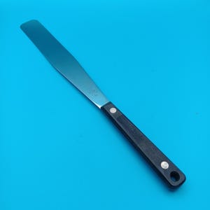 May include: A stainless steel offset spatula with a black handle. The blade is long and rectangular, ideal for frosting cakes and other baking tasks. The handle has a hole for hanging.