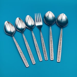 May include: A set of six stainless steel flatware pieces consisting of five spoons and one fork. Each handle features a raised floral pattern with small flowers and scrolling vines. The utensils have a polished metallic finish and straight handles.