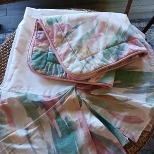 May include: A bed set featuring a white sheet and a patterned comforter and pillowcase. The comforter and pillowcase have a white background with colorful brushstroke designs in shades of pink, green, and yellow. The comforter is trimmed with a pink border.