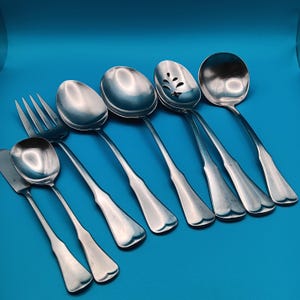 May include: A collection of vintage silverware, including spoons, forks, and serving utensils. The pieces are made of shiny silver metal and arranged on a blue background. The set includes a slotted spoon, a serving spoon, and a cake server.