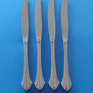 May include: Four silver dinner knives with fluted handles. The knives are arranged in a row on a blue background.