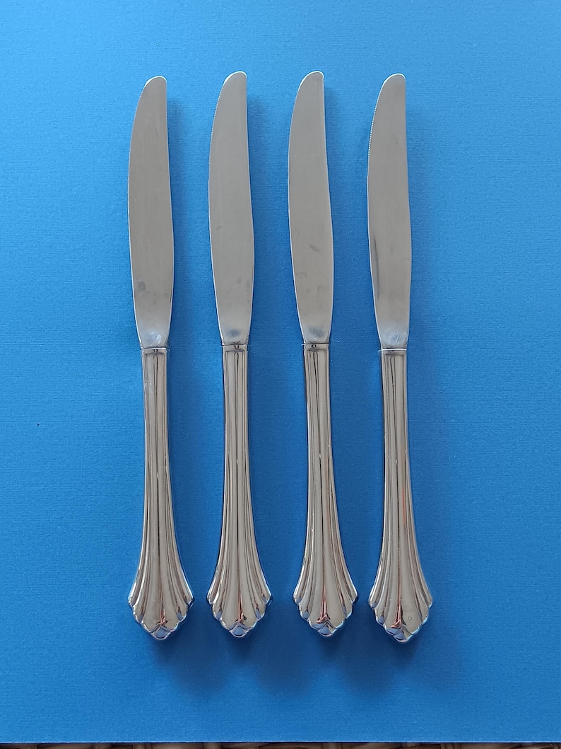 May include: Four silver dinner knives with fluted handles. The knives are arranged in a row on a blue background.