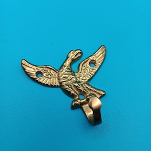 May include: A gold-toned metal wall hook shaped like an eagle with its wings spread wide. The eagle figure features detailed feather textures and includes three circular mounting holes integrated into the wings and base for installation.