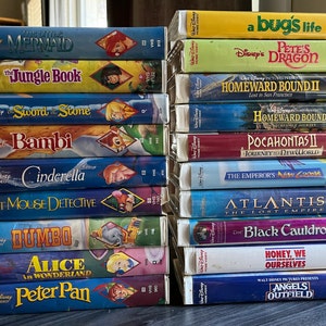 May include: A stack of VHS tapes featuring classic Disney films, including The Little Mermaid, The Jungle Book, Sword in the Stone, Bambi, Cinderella, The Great Mouse Detective, Dumbo, Alice in Wonderland, Peter Pan, a bug's life, Pete's Dragon, Homeward Bound II, Homeward Bound, Pocahontas II, Journey to the New World, The Emperor's New Groove, Atlantis: The Lost Empire, The Black Cauldron, Honey, We Shrunk Ourselves, and Angels in the Outfield.