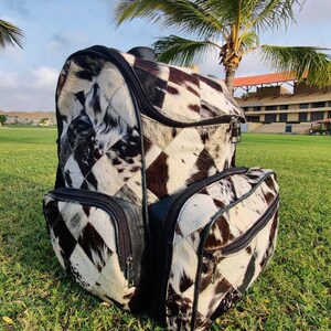 May include: A black and white patchwork leather backpack with multiple zippered compartments. The backpack is made of cowhide and has a unique, stylish design.