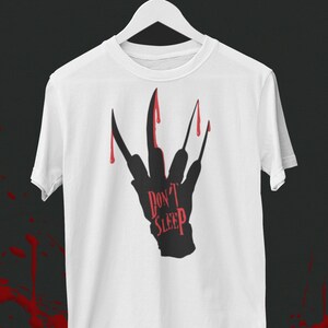 K&ouml;nnte beinhalten: Wei&szlig;es T-Shirt mit einer schwarzen Silhouette einer Hand mit Krallen und tropfendem Blut. Der Text "Don't Sleep" ist auf die Hand geschrieben.