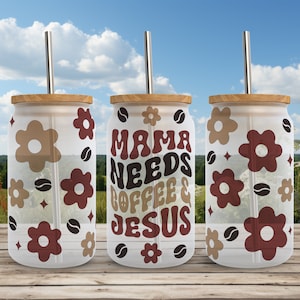 Może przedstawiać: Trzy szklane kubki z bambusowymi pokrywkami i stalowymi słomkami. Kubki mają białe tło z brązowymi ziarnami kawy i czerwonymi i brązowymi kwiatami. Środkowy kubek ma napis "Mama Needs Coffee & Jesus" brązowymi i czerwonymi literami.