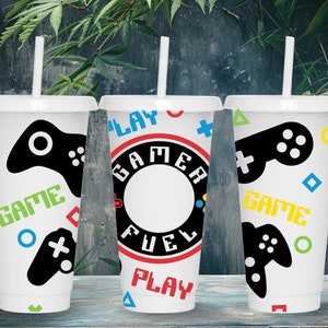 May include: Three white plastic cups with colorful gamer-themed designs. The cups have black and white game controllers, colorful geometric shapes, and the words "Play", "Gamer Fuel", and "Game".