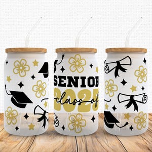 May include: Three white tumblers with black lids and straws. Each tumbler has a different design with black and gold graduation-themed graphics. The designs include a graduation cap, a diploma, stars, and flowers. The text on one tumbler reads "Senior Class of 2021".