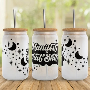 K&ouml;nnte beinhalten: Drei wei&szlig;e Becher mit schwarzen Designs. Der mittlere Becher hat den Text "Manifest that Shit" in einer schwarzen, stilisierten Schrift. Die beiden anderen Becher haben ein Design mit einem Halbmond und Sternen. Jeder Becher hat einen Bambusdeckel und einen Edelstahlstrohhalm.