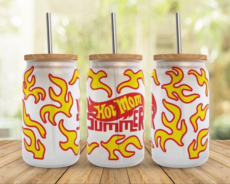 May include: Three white stainless steel tumblers with a wood lid and a straw. The tumblers have a red and yellow flame design and the middle tumbler has the text "Hot Mom Summer" in red and yellow.