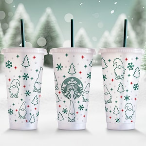 Può includere: Tre bicchieri riutilizzabili bianchi con motivi natalizi verdi e rossi. I bicchieri presentano un fiocco di neve, un albero di Natale e un gnomo. I bicchieri sono riempiti con un liquido bianco e hanno una cannuccia verde.