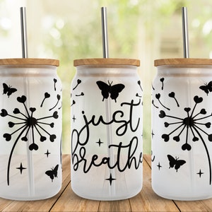 K&ouml;nnte beinhalten: Drei wei&szlig;e Glasbecher mit schwarzen Designs. Die Becher haben Bambusdeckel und Edelstahlstrohhalme. Die Designs beinhalten einen L&ouml;wenzahn mit Herzen, einen Schmetterling und den Text "just breathe".
