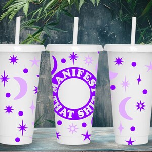 May include: Three white reusable cups with purple and white designs. The middle cup has the text "MANIFEST THAT SH*T" in a purple circle.