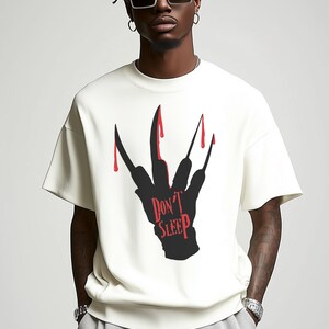 K&ouml;nnte beinhalten: Wei&szlig;es T-Shirt mit einer schwarzen Silhouette einer Hand mit blutigen Krallen und dem Text "Don't Sleep" in Rot.