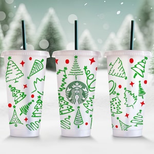 May include: Three white reusable cups with green and red Christmas tree designs. The centre cup has a Starbucks logo with a woman's face.