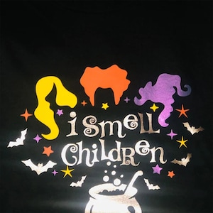 May include: A black t-shirt with a silver glitter design featuring three witches with the text "I smell children" and a cauldron with bubbling liquid.