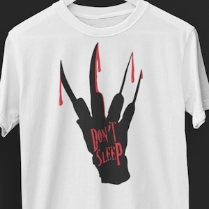 K&ouml;nnte beinhalten: Wei&szlig;es T-Shirt mit einer schwarzen Silhouette einer Hand mit blutigen Krallen und dem Text "Don't Sleep" in Rot.