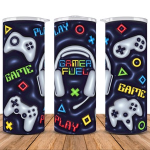 Może przedstawiać: Czarny i niebieski kubek z motywem gier. Prezentuje kontroler do gier wideo, słuchawki i słowa "Game", "Play" i "Gamer Fuel".