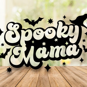 May include: Black and white illustration of the text "Spooky Mama" with bats and stars on a blurred green background.