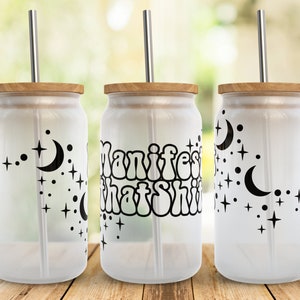 May include: Three frosted glass tumblers with bamboo lids and metal straws. The tumblers have black and white designs. One tumbler has the text "Manifest That Shit" in a retro font. The other two tumblers have a crescent moon and stars design.