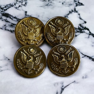 May include: Four gold-coloured metal buttons with the US seal embossed on each. The seal features an eagle with outstretched wings, a shield, and a banner.