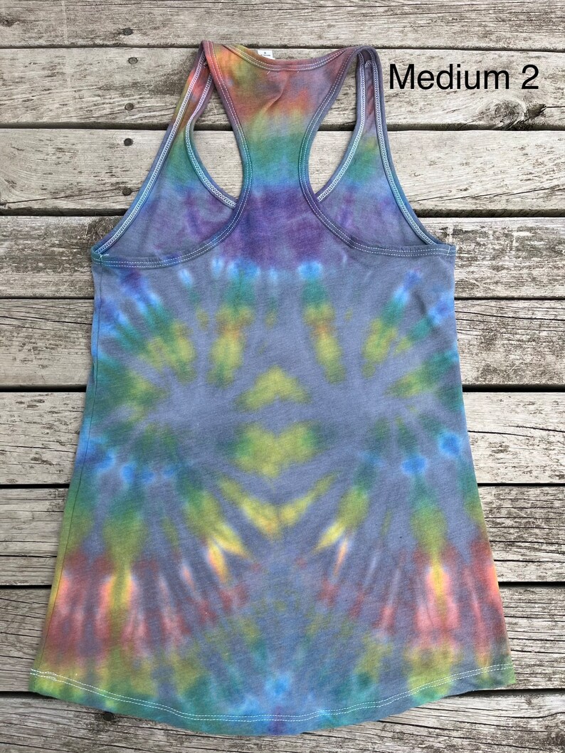 K&ouml;nnte beinhalten: Batik-Tanktop mit einem Regenbogenmuster in Blaut&ouml;nen, Gr&uuml;n, Gelb, Orange und Lila. Das Tanktop hat einen Racerback-Stil und ist mit "Medium 2" gekennzeichnet.