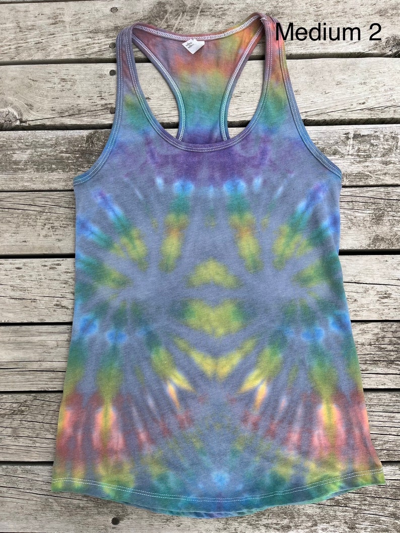 K&ouml;nnte beinhalten: Ein Batik-Tanktop mit einem Regenbogenmuster in Blaut&ouml;nen, Gr&uuml;n, Gelb, Orange und Rosa. Das Tanktop hat einen Racerback-Stil und ist aus einem weichen, bequemen Stoff gefertigt. Der Text "Medium 2" ist in der oberen rechten Ecke des Bildes sichtbar.