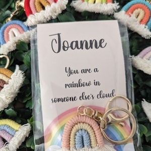 May include: A rainbow keychain with a white fluffy cloud and a gold key ring. The keychain is packaged with a card that reads "Joanne You are a rainbow in someone else's cloud."