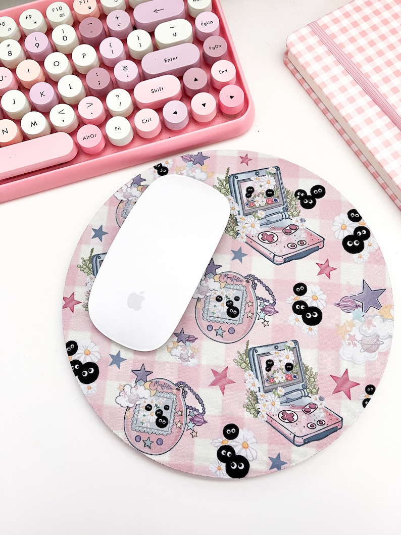 May include: A pink and white checkered mouse pad with a repeating pattern of a pink and white handheld game console, stars, and black eyes. A white wireless mouse is on top of the mouse pad.