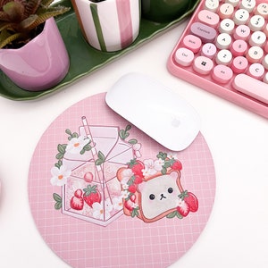 May include: A pink round mousepad with a grid pattern features a cartoon illustration of a glass of milk with strawberries and a bear-shaped piece of toast with strawberries.