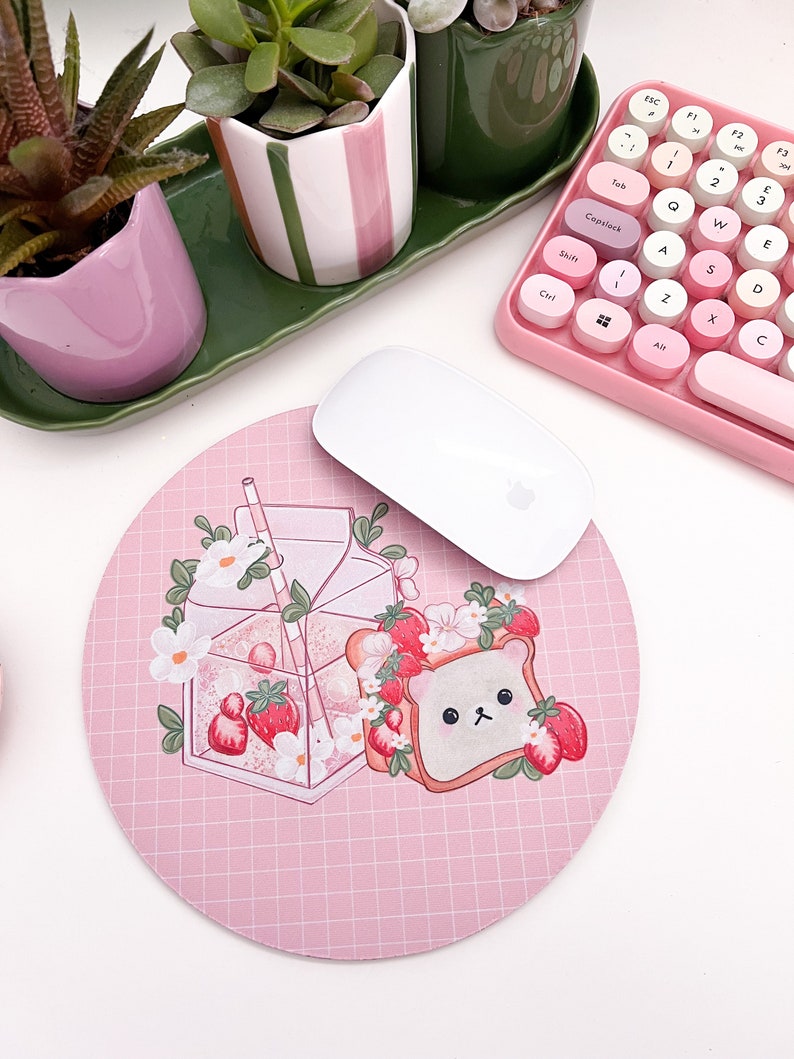 May include: A pink round mousepad with a grid pattern features a cartoon illustration of a glass of milk with strawberries and a bear-shaped piece of toast with strawberries.