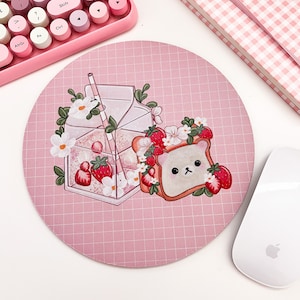 May include: A pink round mousepad with a grid pattern. The mousepad features a cartoon illustration of a carton of milk with a straw, a slice of bread with a bear face, and strawberries.