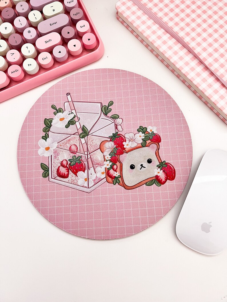 May include: A pink round mousepad with a grid pattern. The mousepad features a cartoon illustration of a carton of milk with a straw, a slice of bread with a bear face, and strawberries.