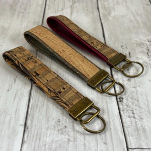 May include: Three cork keychains with different patterns and gold-toned key rings. The keychains are made of cork and have a brown, beige, and black color scheme.