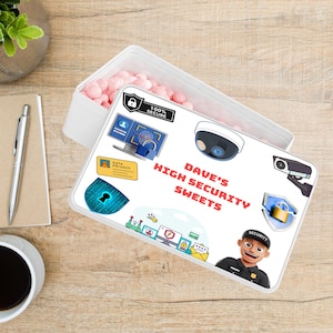 May include: A white rectangular container filled with pink sweets. The lid is decorated with security-themed illustrations, such as a padlock, a computer screen, and the words "DAVE'S HIGH SECURITY SWEETS."