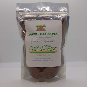 May include: A clear plastic bag filled with brown broccoli sprout seeds. The bag has a white label with the text "COUNTRY CREEK ACRES", "GROWING IS IN OUR ROOTS", "Broccoli Sprouts", "MICROGREENS", "*Non GMO *100% Seed", and "*Produced and Packaged in USA".