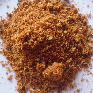 May include: A close-up of a pile of brown and orange spice blend on a white surface.