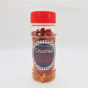 May include: A clear glass jar with a red lid filled with crushed red pepper flakes. The jar has a black and white checkered label with the text "Crushed Red Pepper" in red and white.