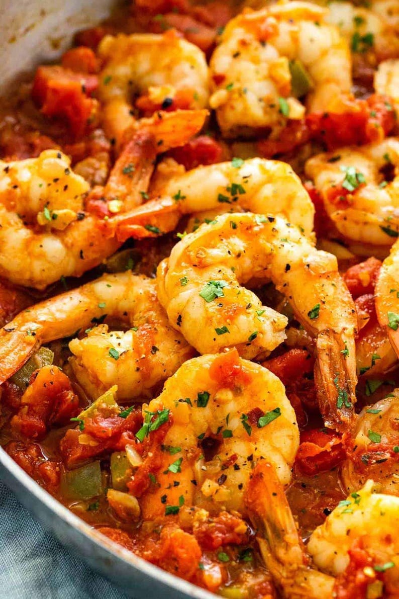 May include: A close-up of a skillet filled with cooked shrimp in a tomato sauce. The shrimp are plump and juicy, and the sauce is rich and flavorful. The shrimp are garnished with fresh parsley.