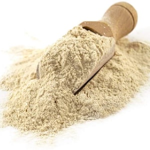 May include: A scoop of light beige powder, likely a type of flour, sits on a wooden scoop. The powder is piled high and spills over the sides of the scoop.