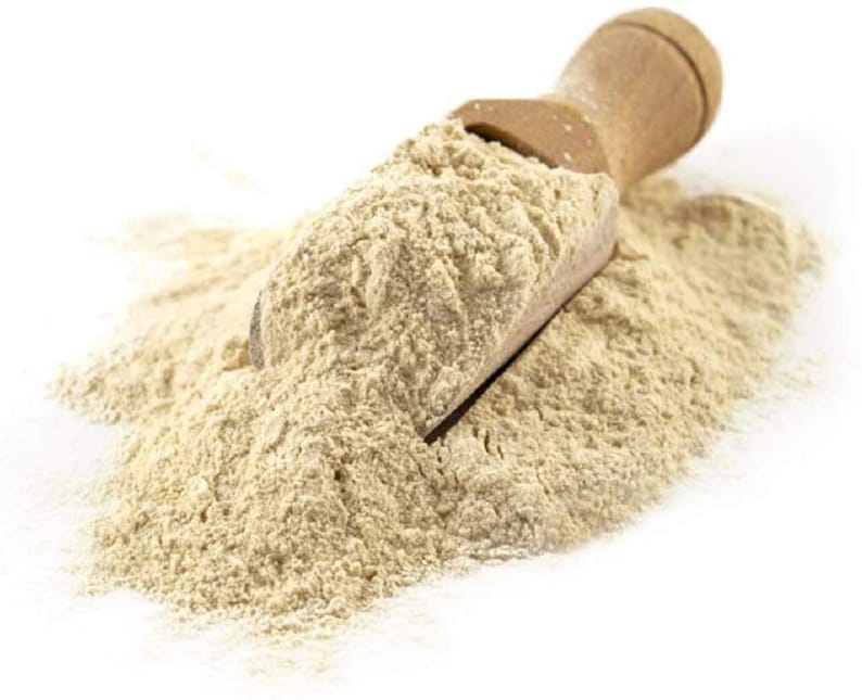 May include: A scoop of light beige powder, likely a type of flour, sits on a wooden scoop. The powder is piled high and spills over the sides of the scoop.