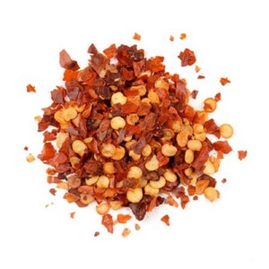 May include: A close-up of a pile of red pepper flakes and seeds. The flakes are a mix of red and orange, and the seeds are a light yellow.