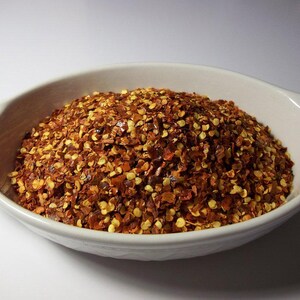 May include: A white ceramic bowl filled with red pepper flakes. The flakes are a mix of red and yellow.