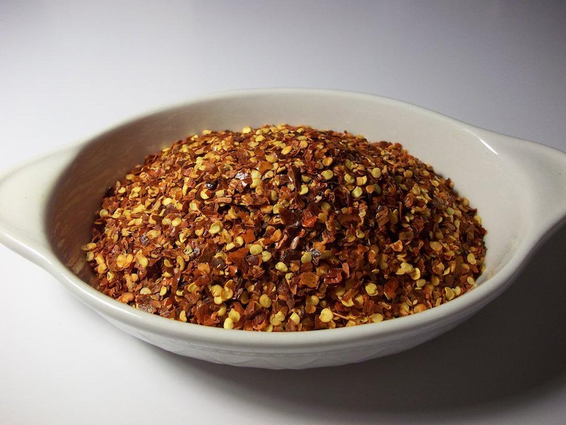 May include: A white ceramic bowl filled with red pepper flakes. The flakes are a mix of red and yellow.