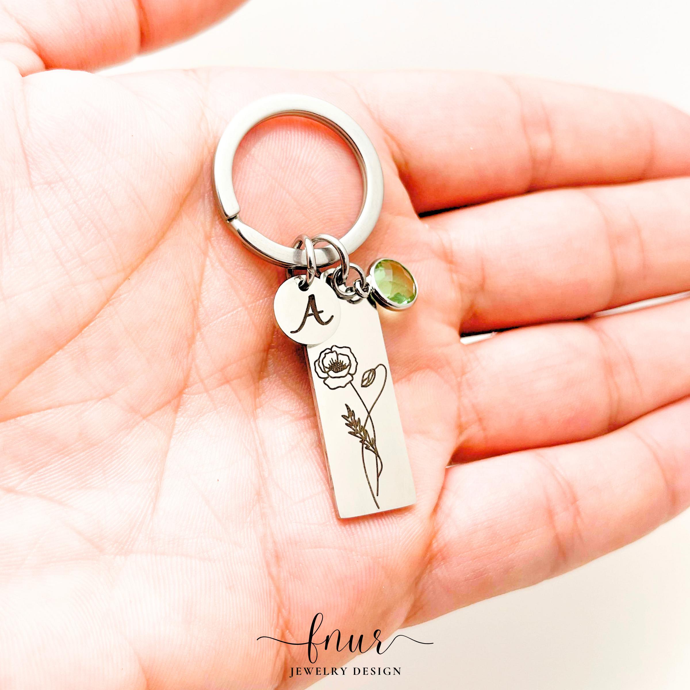 Handheld close up showing gold finish birth flower keychain with personalized name engraving detail