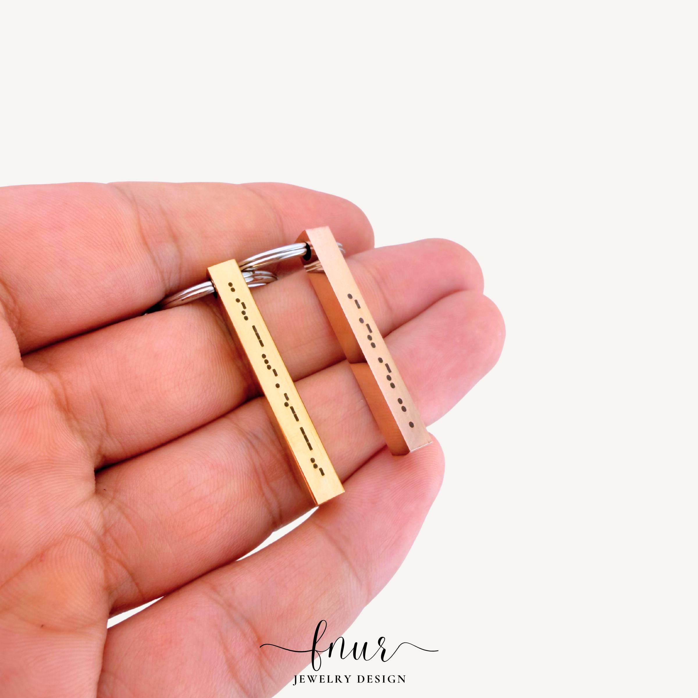 gold finish morse code bar keychain variant reflecting soft light on textured fabric background