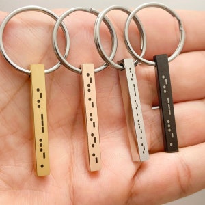 May include: Four keychains with different colored metal bars. Each bar has a different message written in braille.