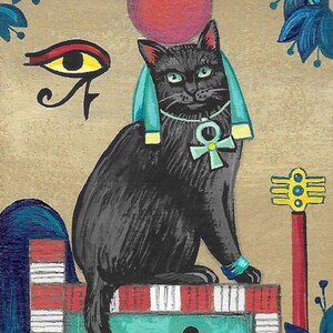 Op de afbeelding: Een zwarte kat met een turquoise hoofdtooi en een ankh-ketting zit op een rood-wit gestreept platform. De kat heeft een rood oog en een geel oog. De achtergrond is beige met een rode cirkel en blauwe bladeren.