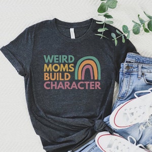 May include: A dark grey t-shirt with the text "Weird Moms Build Character" in colourful letters with a rainbow graphic.
